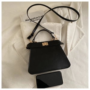 Top-down view of black trapezoid handbag with gold clasp and phone for size reference