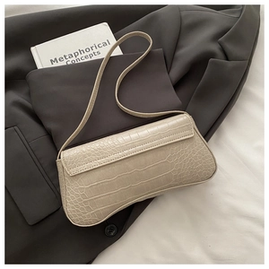 Detailed view of beige crocodile embossed baguette bag on dark grey blazer background