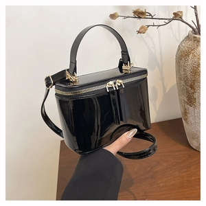 Detailed view of black patent leather crossbody bag with dual gold zippers and top handle