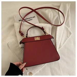 Detail view of the deep red trapezoid handbag featuring a gold-toned twist lock closure