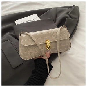 Detail view of beige crocodile embossed baguette bag with golden oval twist-lock closure