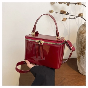 Detail of wine red patent leather box bag with dual zippers and a glossy finish