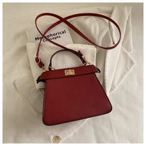 Detail of dark red trapezoid handbag with gold twist lock on white corduroy fabric