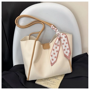 Detail of a creamy tote bag with brown straps and a pink polka dot scarf on a chair