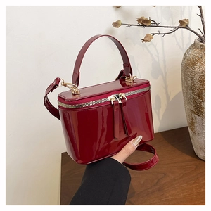 Detail of burgundy patent leather box bag with top handle and golden hardware on wooden surface