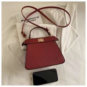 Macro view of burgundy trapezoid handbag with gold rotary lock and size reference phone