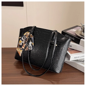 Detail of black faux crocodile leather tote bag with elegant floral scarf on the handle