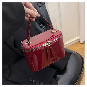 Detail of deep red patent leather box bag with gold zipper and top handle
