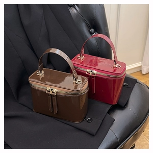 Close-up of elegant glossy patent leather box bags in dark brown and wine red with gold hardware