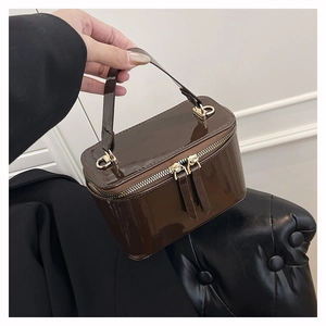 Detail of glossy chocolate patent leather handbag with premium gold hardware and dual zippers