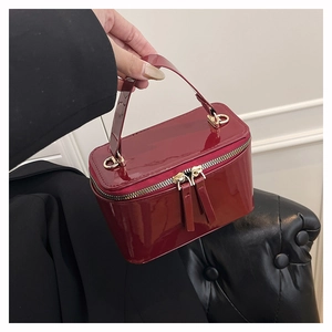 Detail of red patent leather box bag with dual metal zippers held by a model