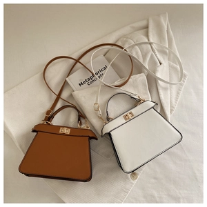 Flat lay detail of brown and white trapezoid handbags with metal twist locks and wing structure