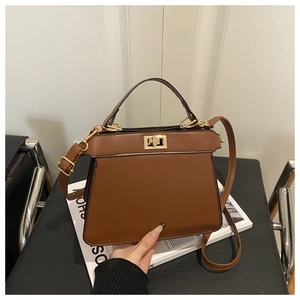 Detail of a brown leather trapezoid handbag featuring a metal twist lock and single handle