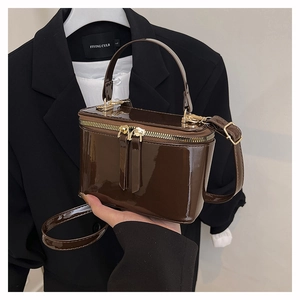 Macro detail of dark brown patent leather box bag with gold double zippers and top handle