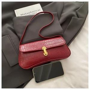Detail of dark red crocodile embossed baguette bag with gold buckle and phone for scale