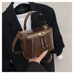 Detailed close-up of dark brown patent leather box bag with gold zipper and top handle