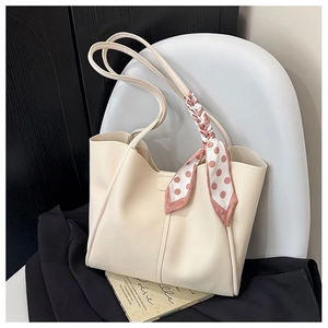 Detail of cream tote bag with polka dot silk scarf handle on a white chair