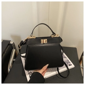 Detail of black trapezoid handbag showing matte leather texture and golden twist lock closure