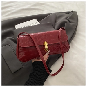 Close-up of red crocodile embossed leather handbag with gold metal clasp on gray suit