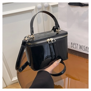 Detail of glossy black patent leather box bag with gold-tone hardware and zippers