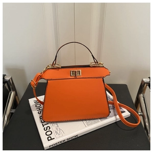 Detail view of a bright orange leather handbag with gold twist lock on a magazine