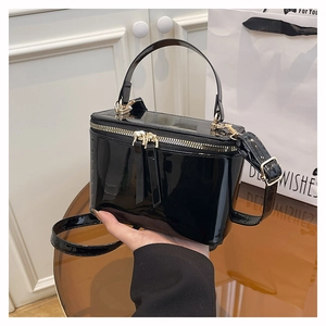 Detail of black patent leather box bag with gold metal zippers and top handle
