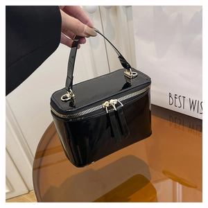 Detail of glossy black patent leather trapezoid box bag with dual gold zippers