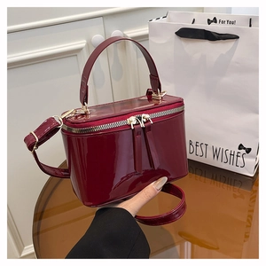 Detailed view of burgundy patent leather box bag with top handle and gold hardware