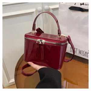 Detail of burgundy patent leather box bag featuring gold double zippers and top handle