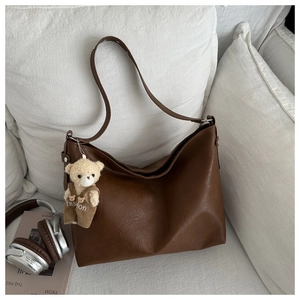Detail of deep brown tote bag featuring leather texture and a cute bear bag charm