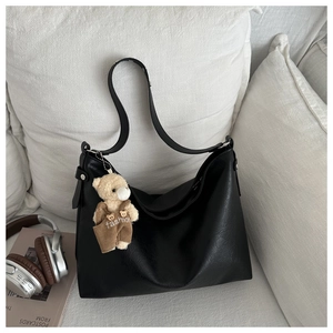Detail of minimalist black hobo bag with a cute teddy bear charm on a cozy sofa
