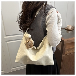 Detail of cream pleated leather hobo bag with a cute teddy bear charm in warm lighting