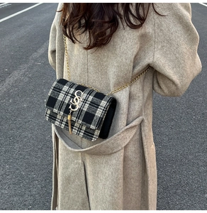 Detail of black and white plaid chain bag with golden logo and tassel on a beige coat