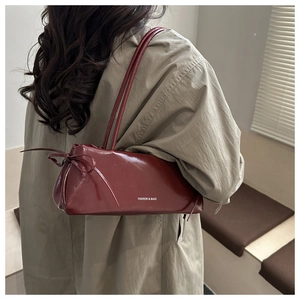 Close-up of a burgundy underarm bag with a glossy finish and stylish bow detail