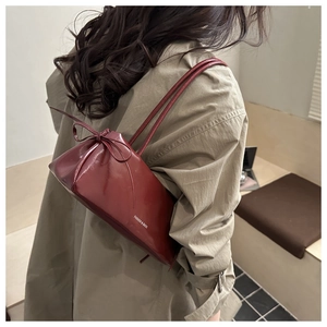 Close-up of shiny dark red leather shoulder bag with bow detail and slim straps