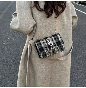 Detail of a black and white plaid crossbody bag with a gold chain and tassel charm