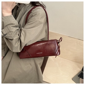 Dettaglio della borsa baguette bordeaux in pelle lucida con nastro laterale e logo bianco