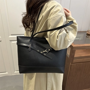 Black pebble leather tote bag with gold lock and metal eyelets shown on a shoulder