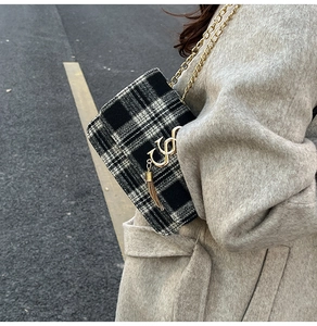 Detail of checkered crossbody bag with gold chain strap and metallic logo pendant