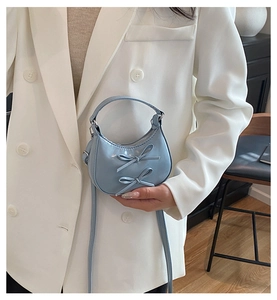 Detail of light blue crescent mini bag featuring twin decorative bows and glossy finish