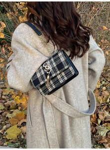 Detail of black and white plaid handbag with golden SS logo and fringe on wool fabric