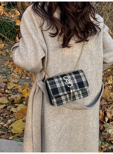 Close-up of black and white plaid handbag featuring a silver S-shaped metal buckle and tassel