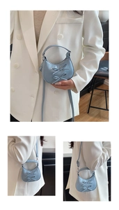 Detail of light blue crescent bag featuring double bow accents and chain strap in macro view