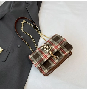 Detail of plaid flap bag with golden logo and fringe tassel on grey suit fabric