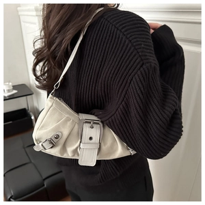 Close-up of beige canvas shoulder bag with buckle detail and pleated texture on a model