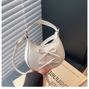 Close-up of cream-white mini hobo bag with bow details on vintage book backdrop