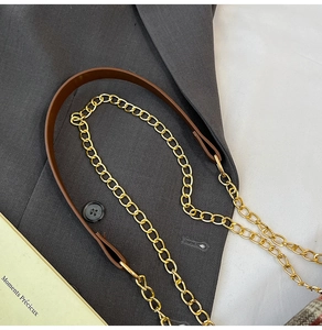 Detail of golden metal chain strap with brown leather connector on a plaid handbag
