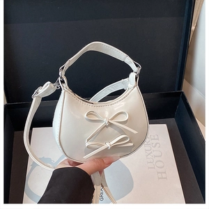 Detail of white crescent bag with double bow decoration and polished PU leather surface