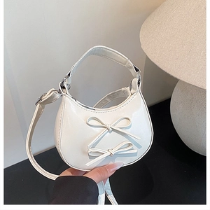 Detail of white mini bow handbag in glossy finish being held for size scale