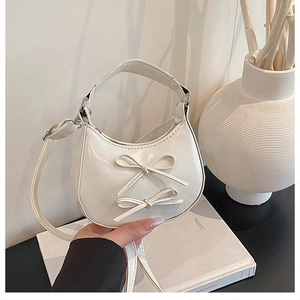 Detail of white crescent bag featuring dual bow accents and polished glossy finish
